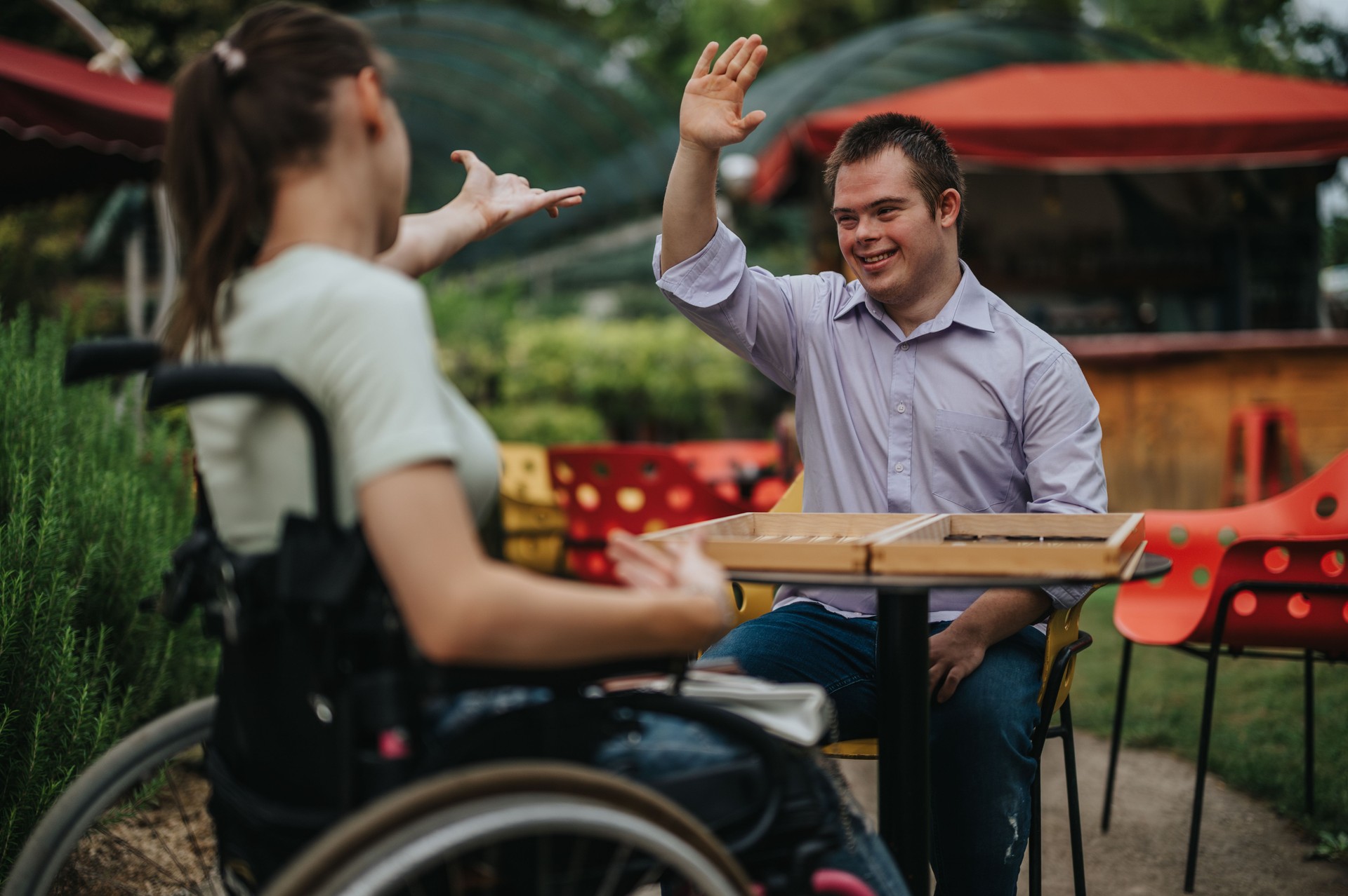 A boy with Down syndrome and a girl in a wheelchair share a joyful moment in a vibrant outdoor setting, demonstrating friendship and inclusion.